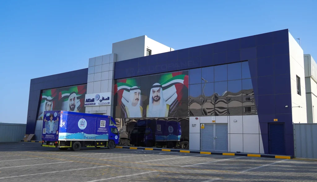 A side-angle view of the AlSafi building showing the prominent Alucopanel branding and large-scale murals of UAE rulers on the glass windows.