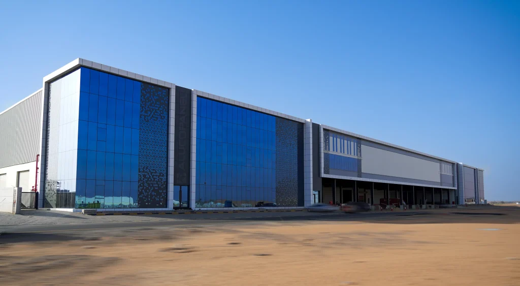 Full elevation of Alucopanel facility main facade featuring blue reflective glazing, white and dark aluminum composite cladding with loading dock bays