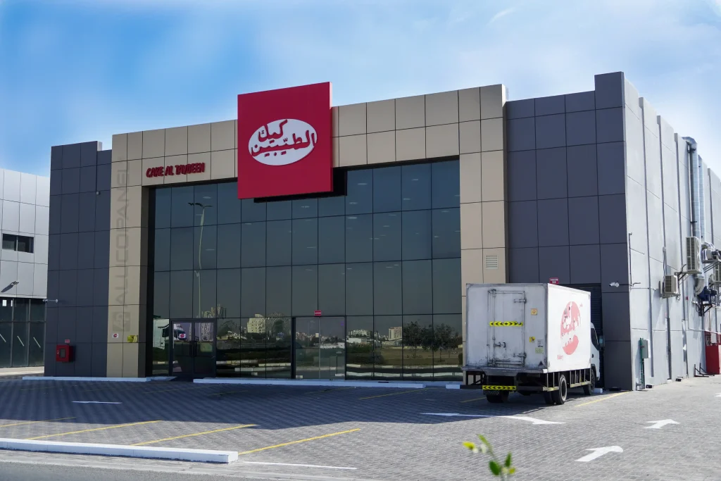 Cake Al Taybeen factory front entrance with red brand signage and Alucopanel cladding in UAE